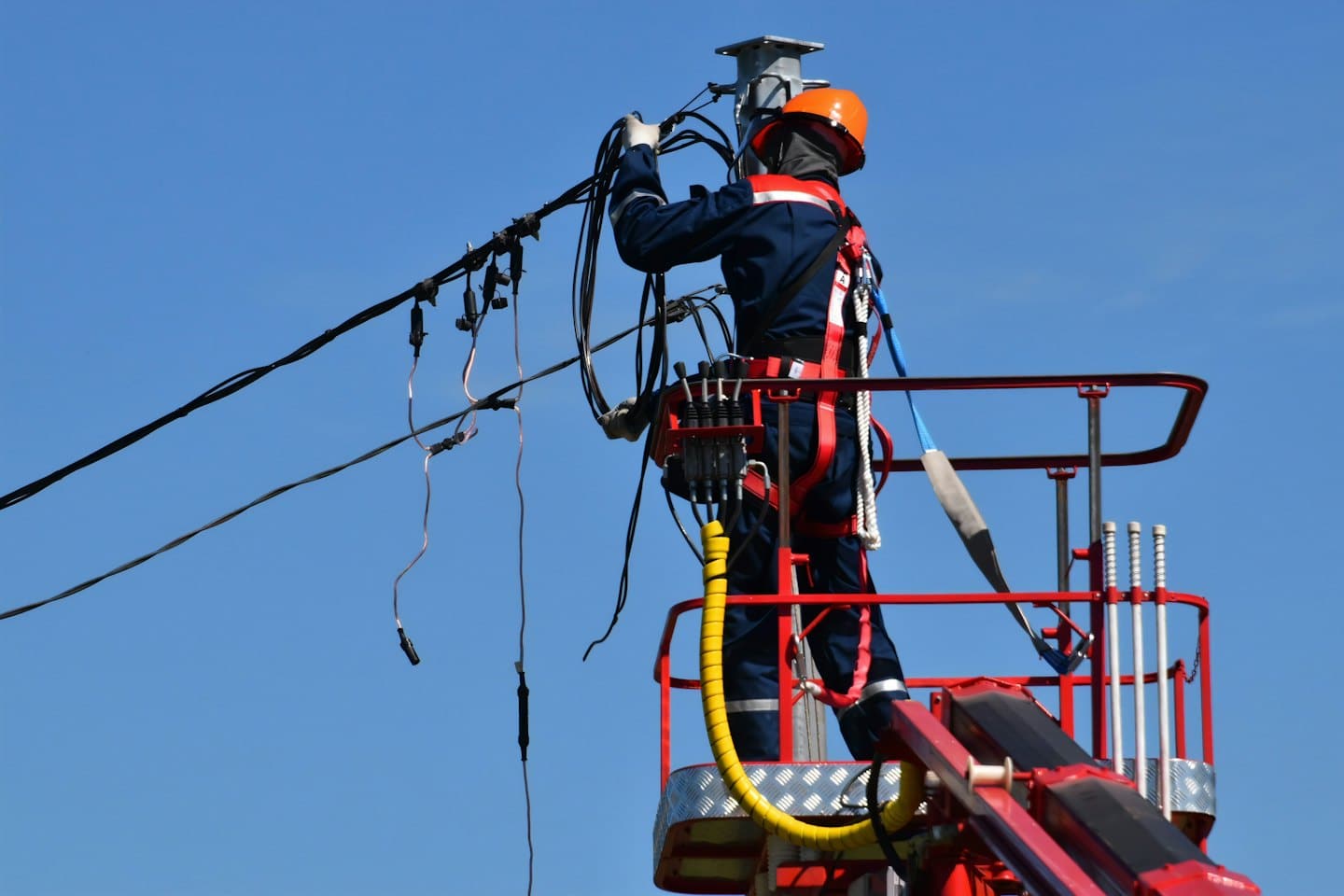 Electrician in orange hard hat works on wires from aerial platform.